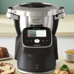 Robot cuiseur Moulinex i-Companion Touch Pro noir posé sur un plan de travail de cuisine, entouré d’une brioche, d’une tarte et d’une soupe