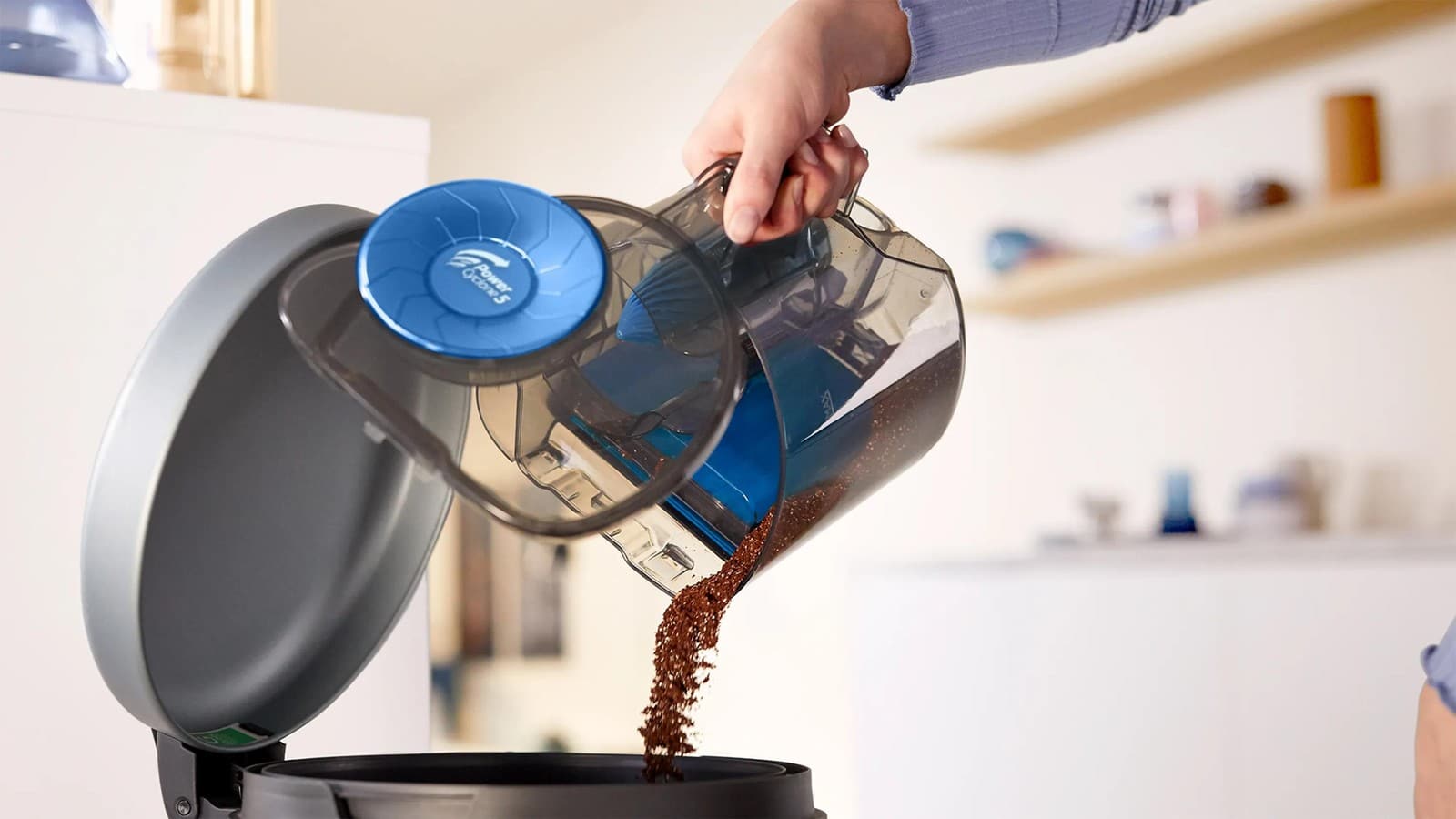 Bac à poussière du Philips PowerPro Compact vidé d’une main au-dessus d’une poubelle