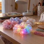 Des chouchous en tissu irisé, une brosse et des barrettes posés sur le bureau d’une chambre d’enfant, éclairés par la lumière d’une fenêtre en automne