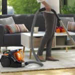 Femme passant l’aspirateur Rowenta Compact Power Cyclonic noir et orange sur un tapis de salon