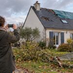 Une habitante photographie le toit bâché et la clôture abattue de sa maison après une tempête