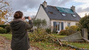 Une habitante photographie le toit bâché et la clôture abattue de sa maison après une tempête